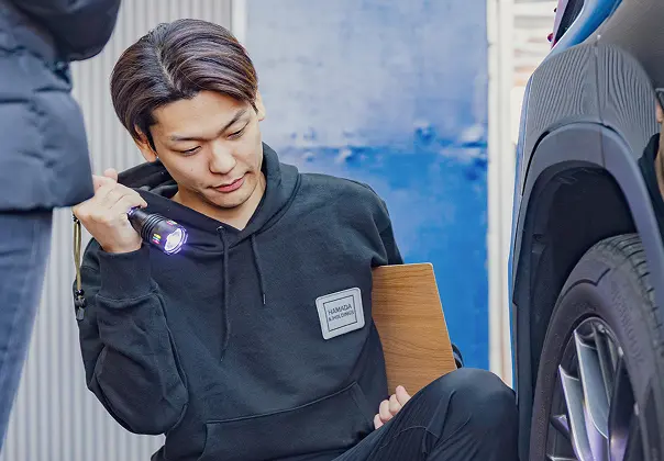 車のタイヤにライトを当てて査定をしている男性の写真